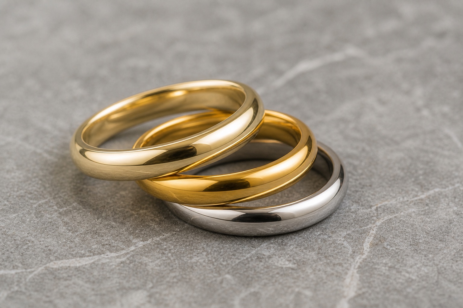 Three ring bands stacked together showing the color gradient from pale 14K yellow gold to rich 18K yellow gold to white metal